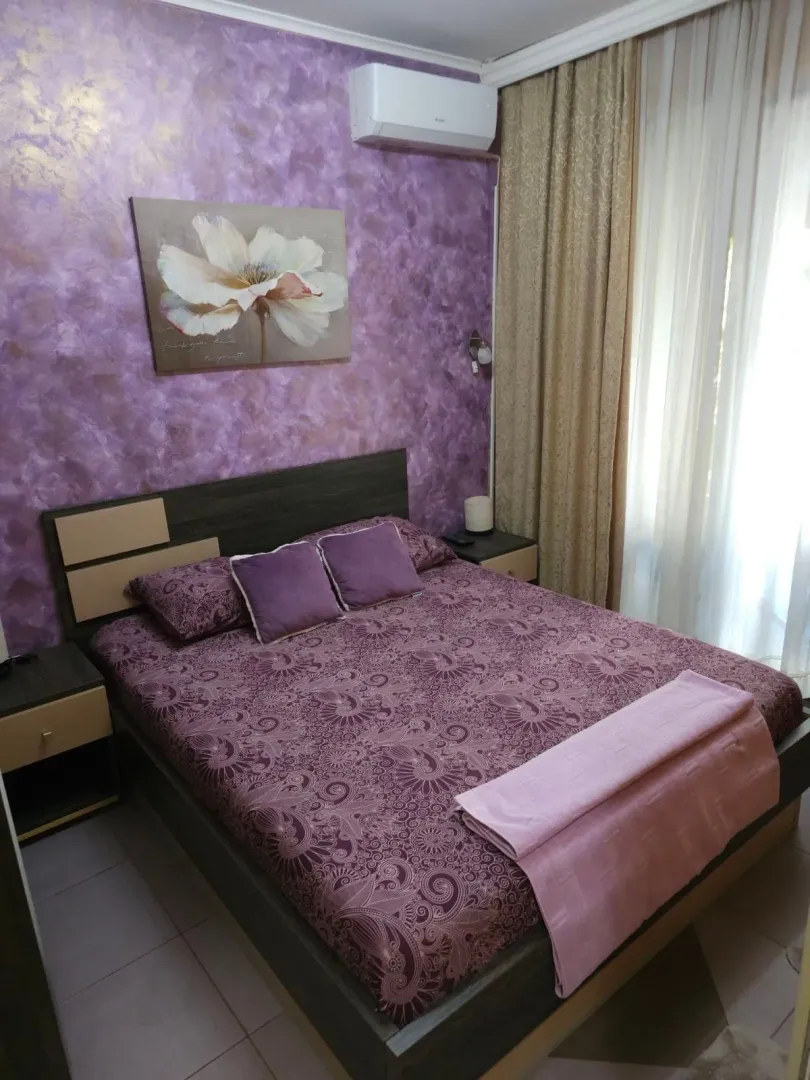 Namještena spavaća soba sa bračnim krevetom i ljubičastim detaljima.