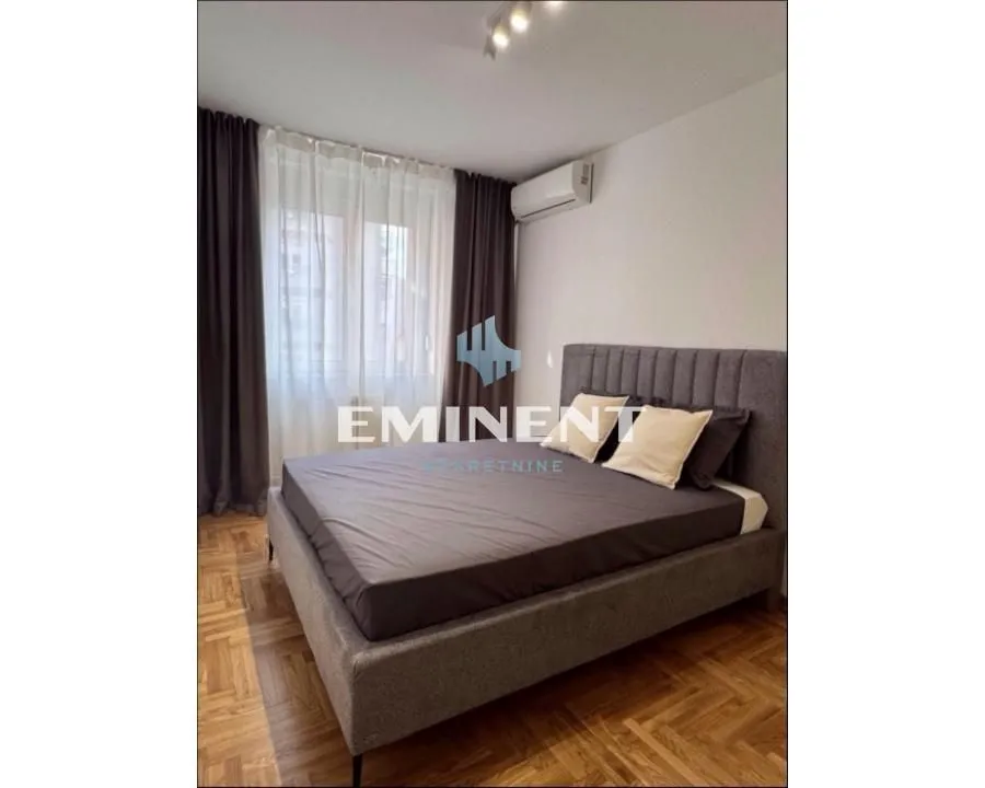 Bedroom with a double bed, parquet flooring, and a window with dark curtains.