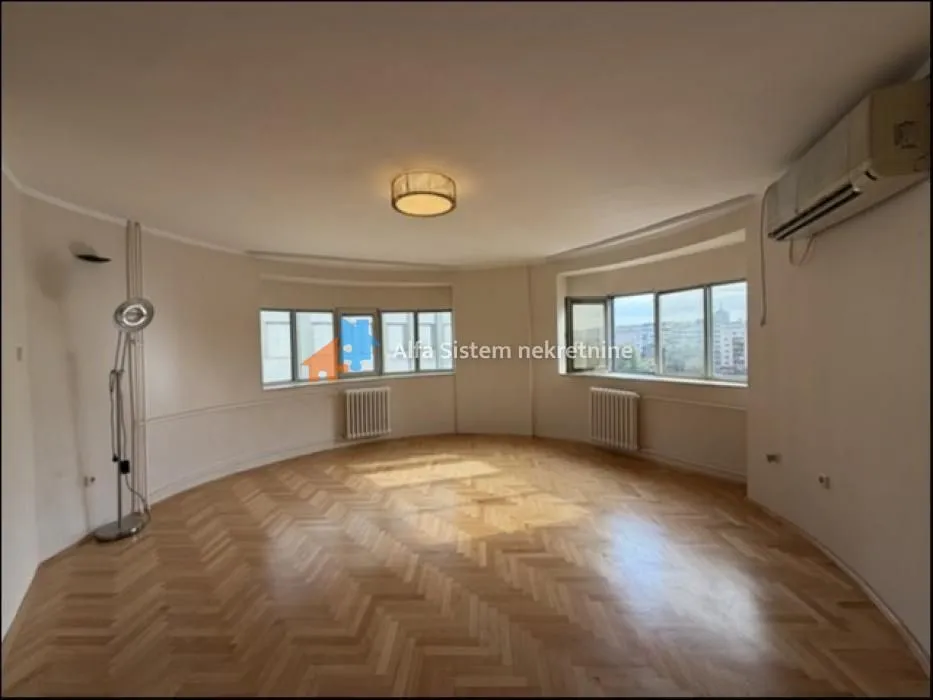 Spacious empty living room with parquet flooring and large windows.