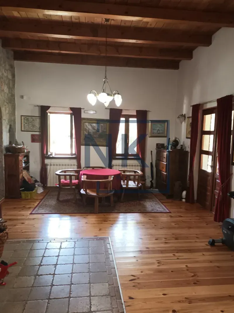 Prostrana dnevna soba sa drvenim gredama na plafonu i trpezarijskim stolom.