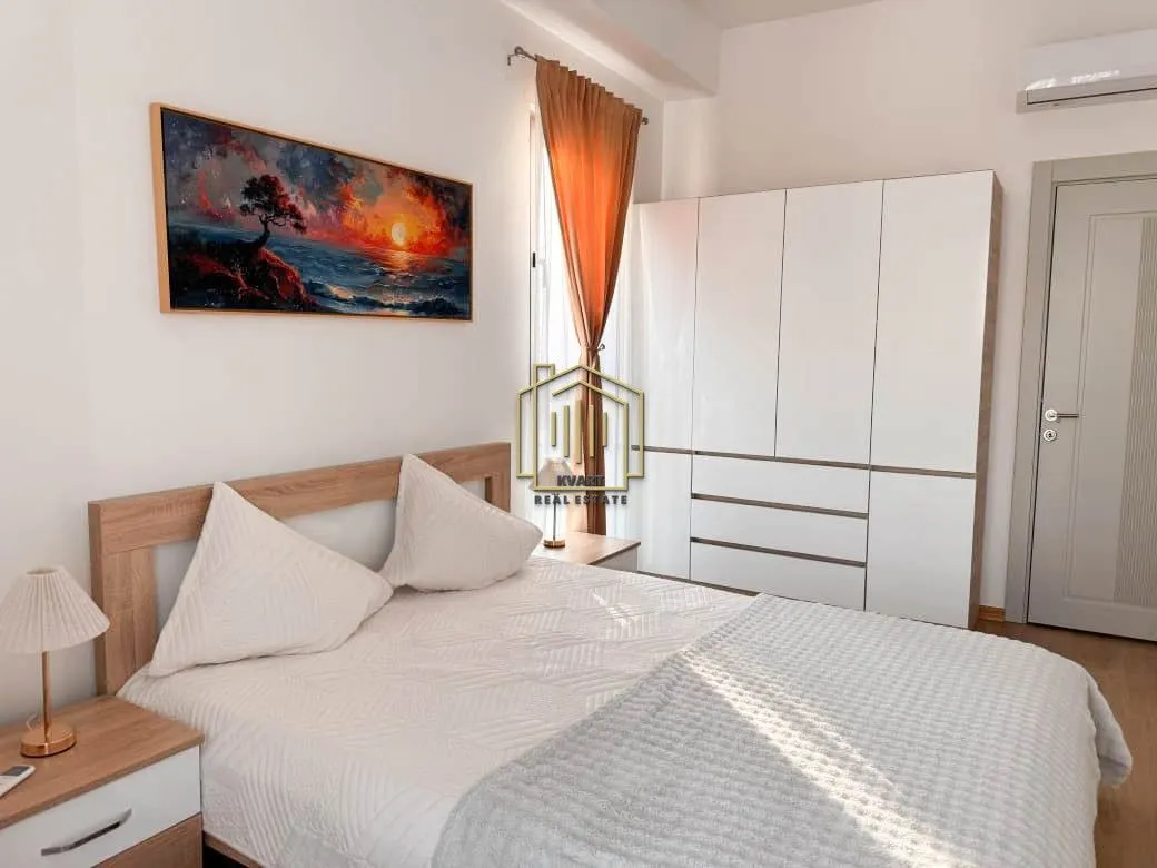Furnished bedroom with a double bed, white wardrobe, and a painting on the wall.