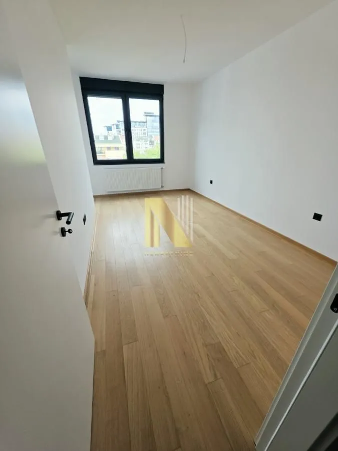 Prazna soba sa parketom i belim zidovima.