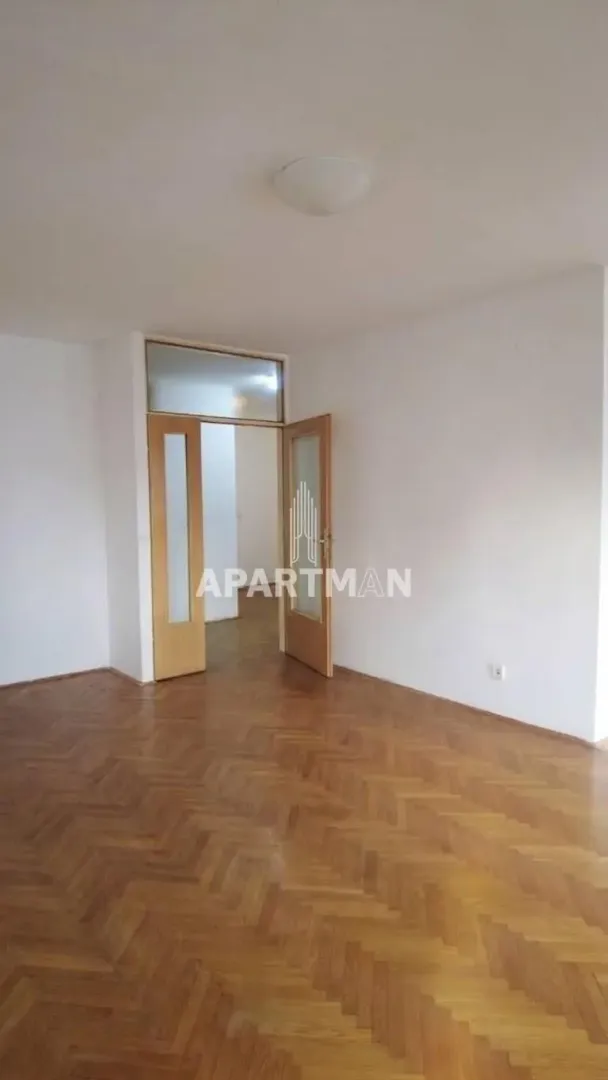 Empty room with hardwood parquet flooring and open double doors.