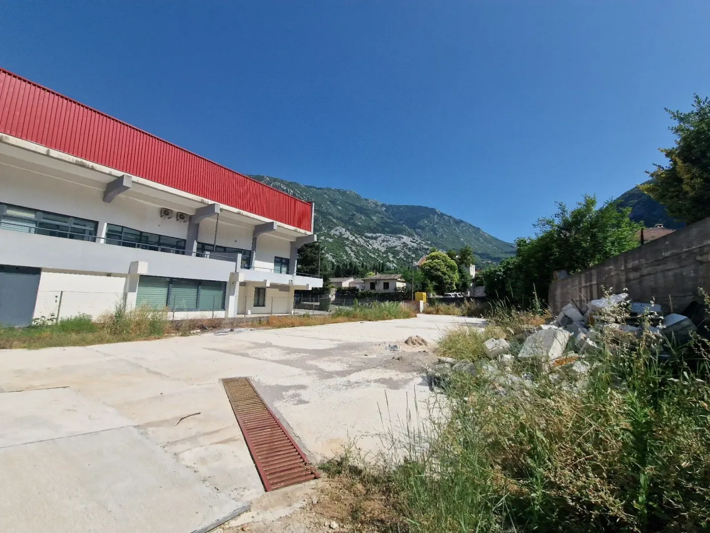 Pogled na spoljašnji dio objekta sa betonskim dvorištem i okolnim pejzažem.