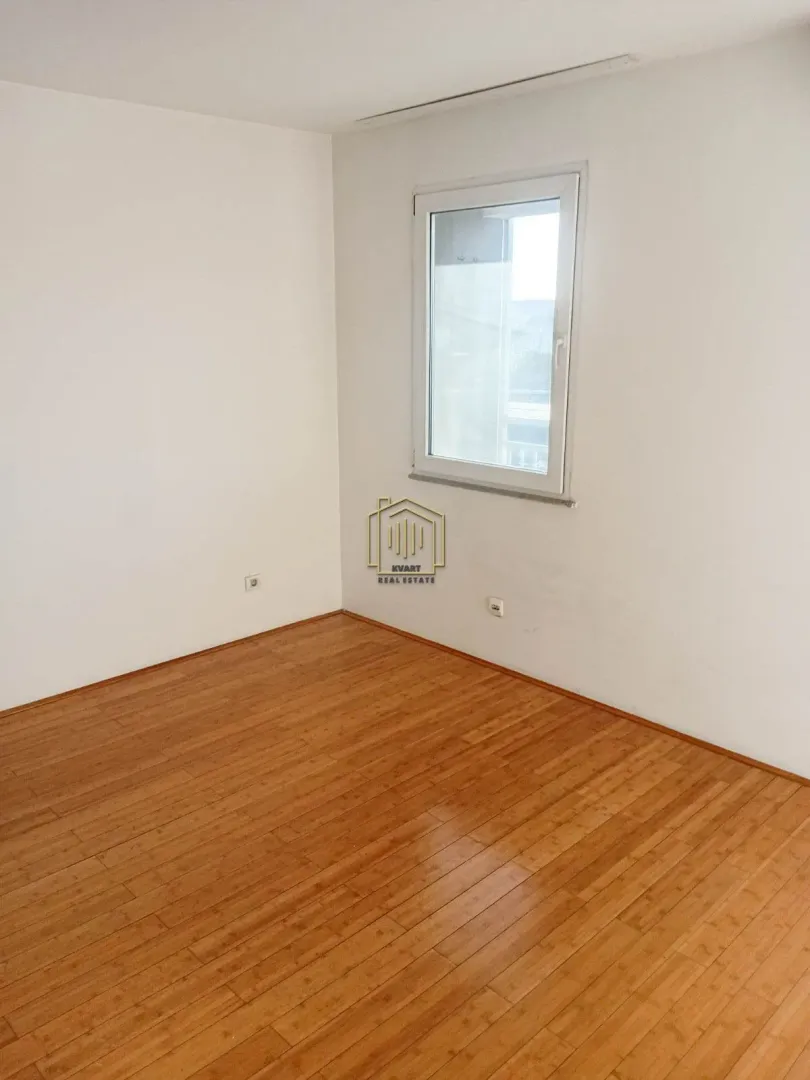 Empty room with white walls, wooden parquet flooring, and a window.