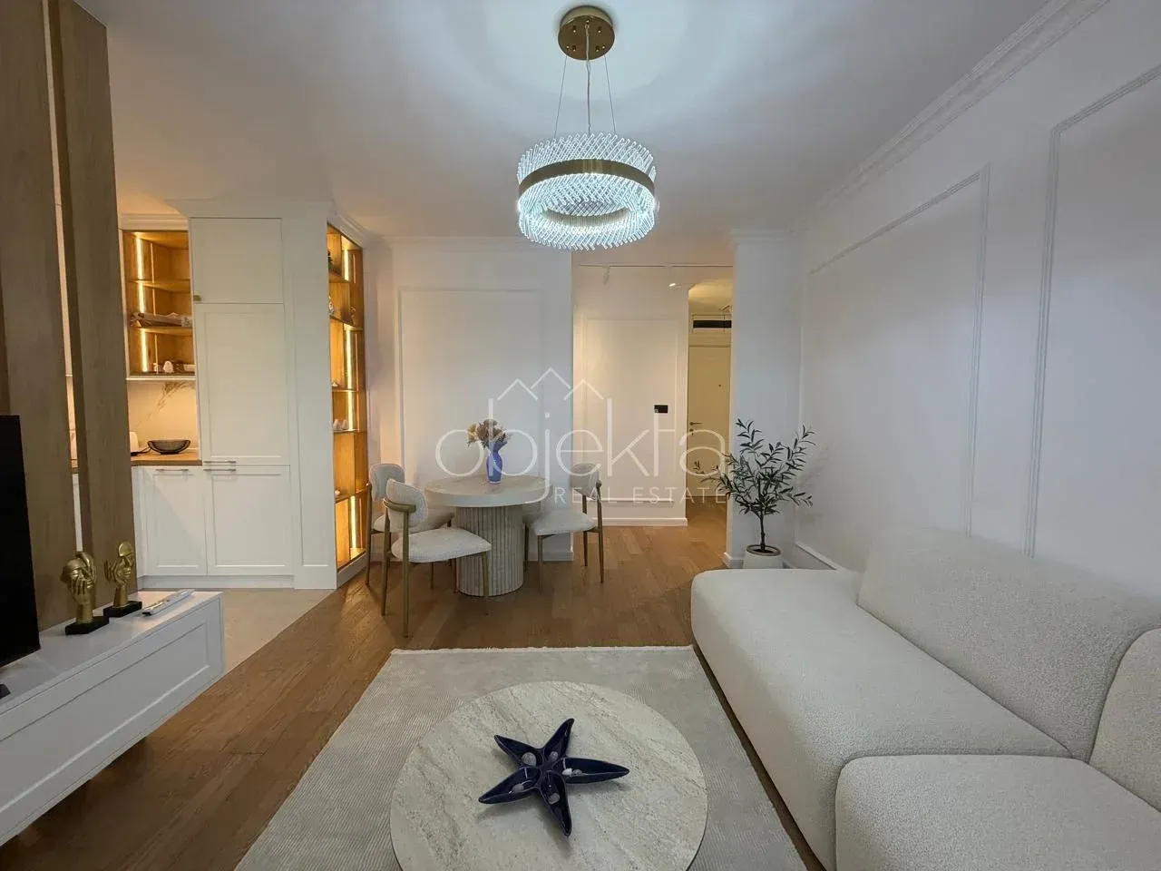 Living room with a sofa, dining area, and part of the kitchen in the background.