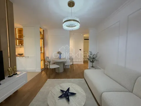 Living room with a sofa, dining area, and part of the kitchen in the background. - image 5