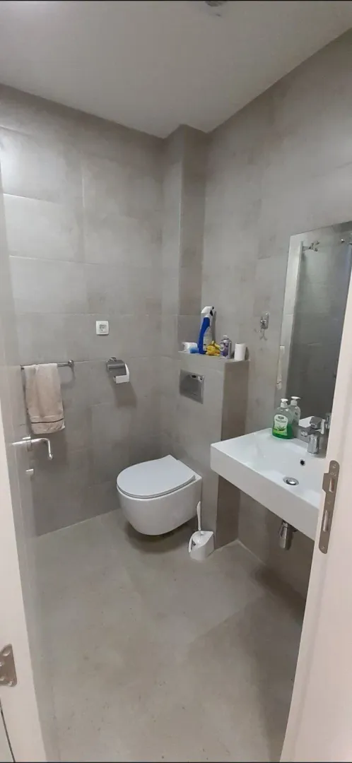 A simple bathroom with grey tiling, a sink, and a toilet.