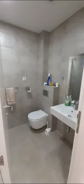 A simple bathroom with grey tiling, a sink, and a toilet. - image 2
