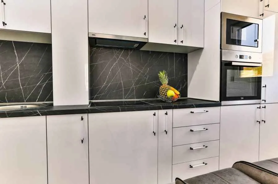 Modern white kitchen with black marble elements and a built-in oven.