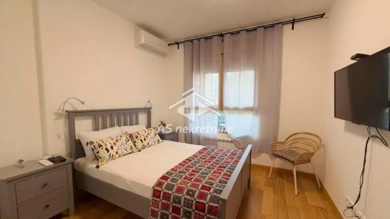 Nameštena spavaća soba sa bračnim krevetom, televizorom i klima uređajem.