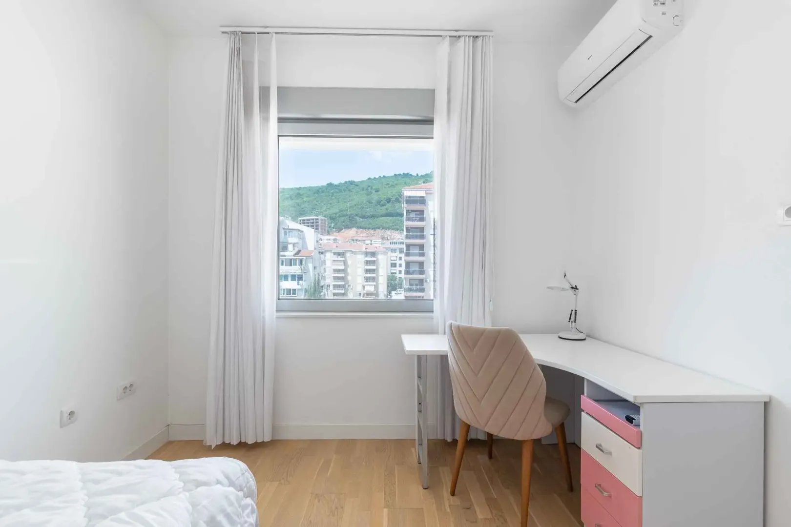 Bright bedroom with a desk and a window overlooking the city.