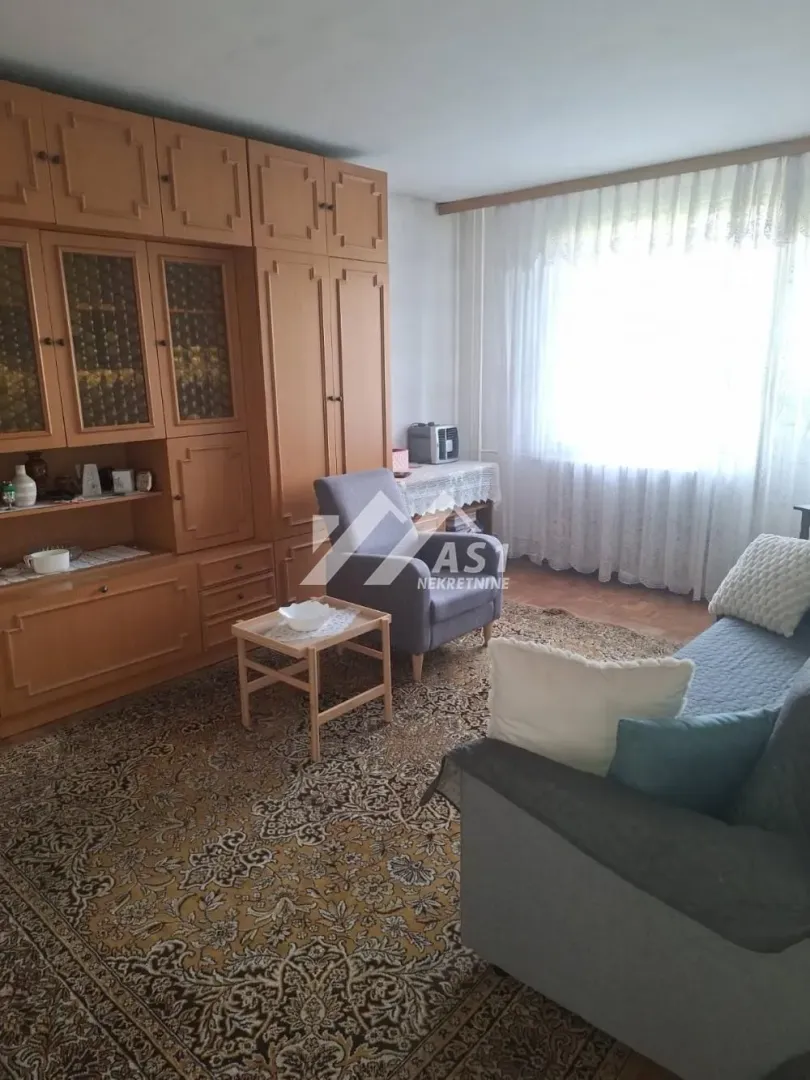 Dnevna soba sa garniturom, foteljom i drvenim ormanom.