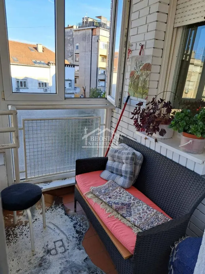 Zastakljeni balkon sa klupom za sedenje i pogledom na okolne zgrade.