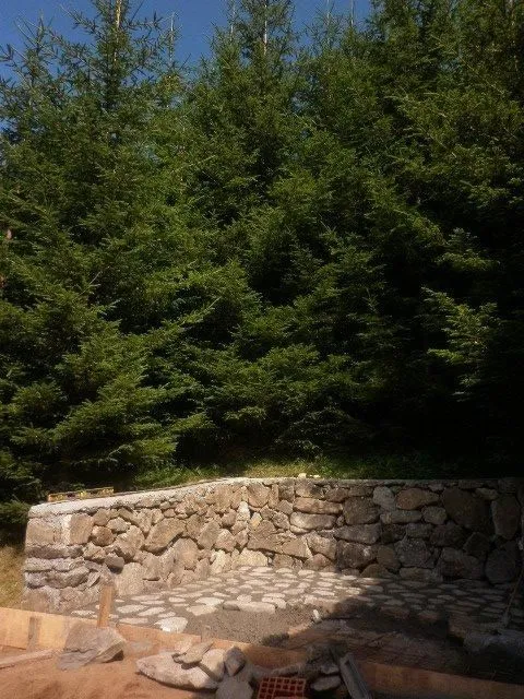 Kameni potporni zid na placu okruženom visokim borovima.