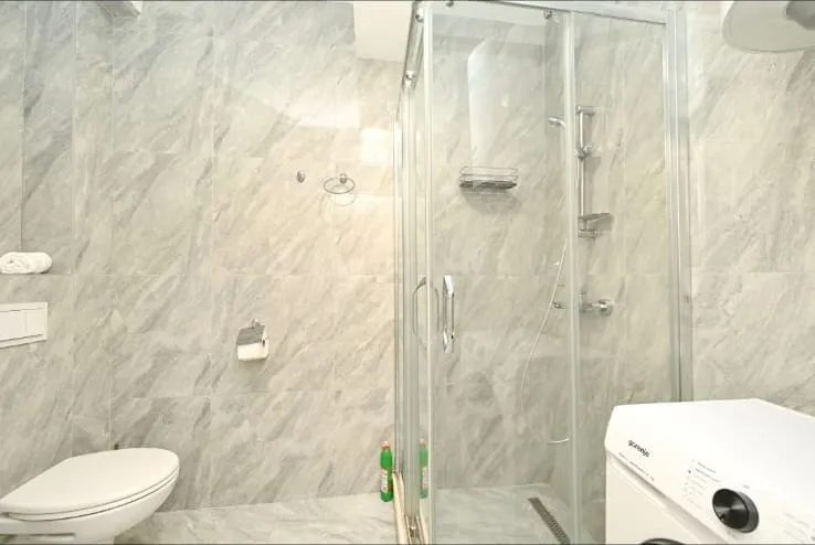 Modern bathroom with a shower cabin, toilet, and washing machine tiled with marble-look tiles.
