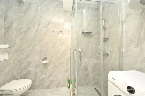 Modern bathroom with a shower cabin, toilet, and washing machine tiled with marble-look tiles. - image 9