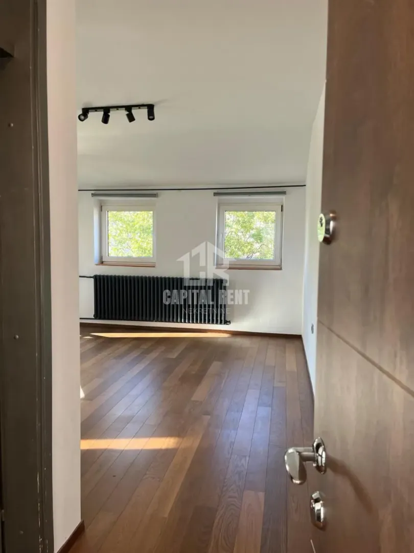 Empty room with wooden flooring, white walls, and two windows.