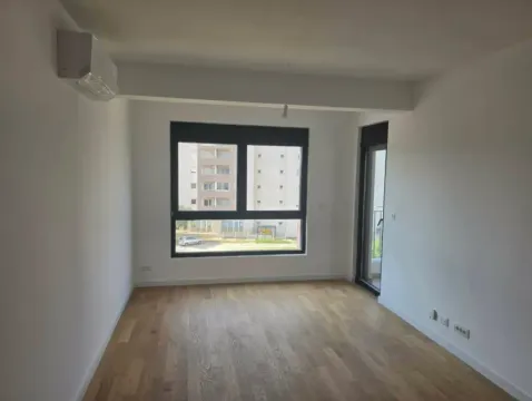 Prazna soba sa drvenim podom, klima uređajem i prozorom koji gleda na susjednu zgradu. - image 5