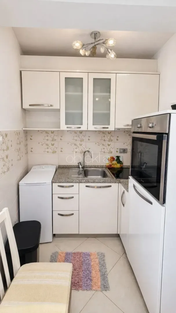 Small white kitchen with a sink, built-in oven, and washing machine.