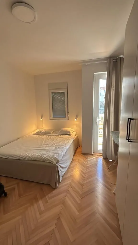 Spavaća soba sa bračnim krevetom, parketom i izlazom na terasu.