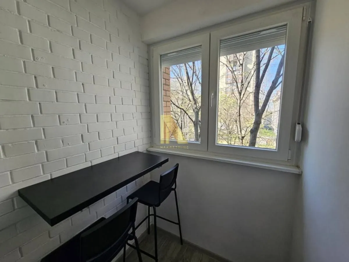 Zastakljeni balkon sa šankom, stolicama i belim ciglama na zidu.