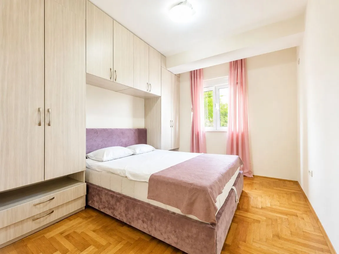 Namještena spavaća soba sa bračnim krevetom i ugradnim plakarima.