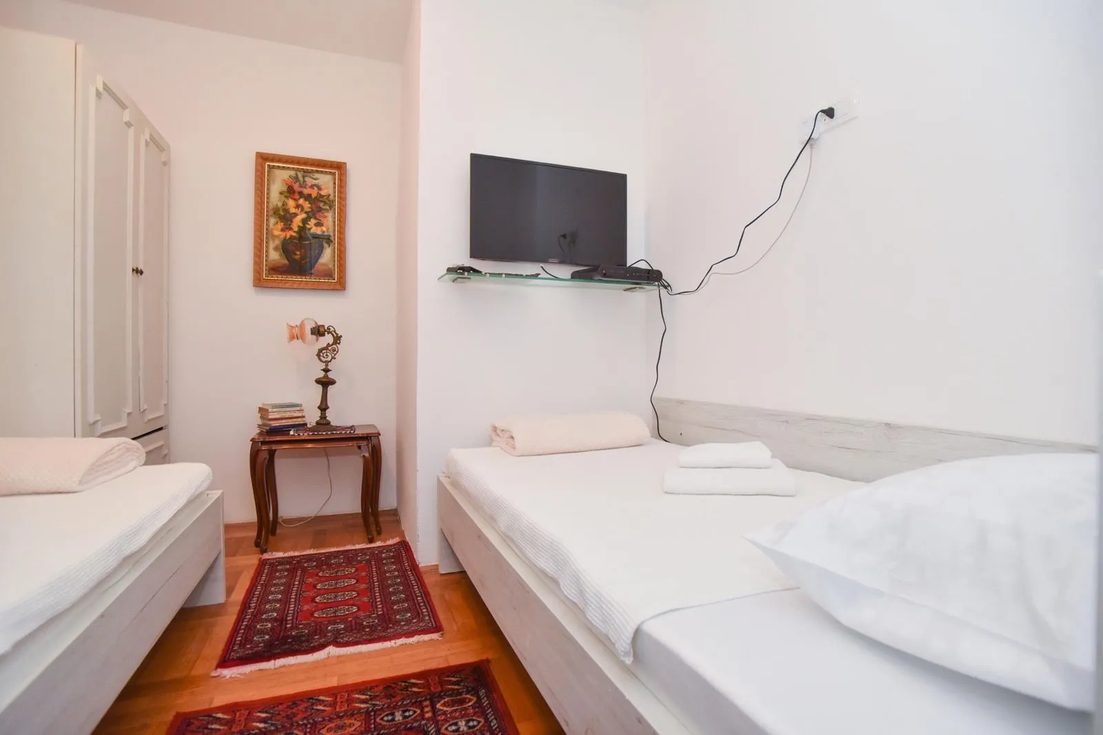 Bedroom with two single beds, a small nightstand, and a wall-mounted TV.