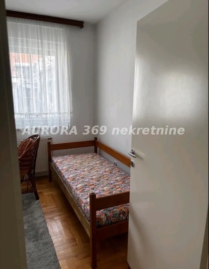Manja spavaća soba sa drvenim krevetom i prozorom sa zavesom.