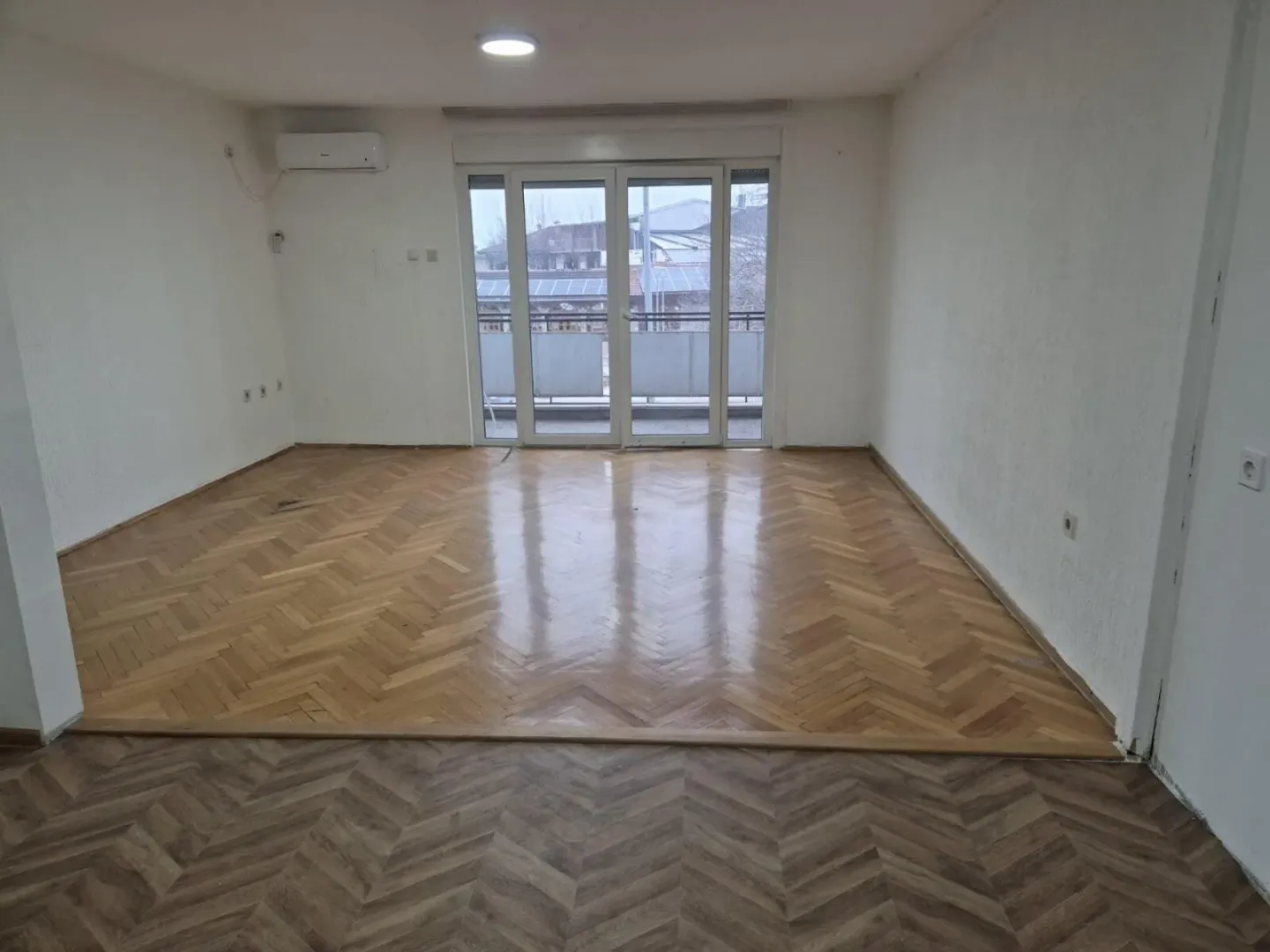 Empty room with parquet flooring and large balcony doors.
