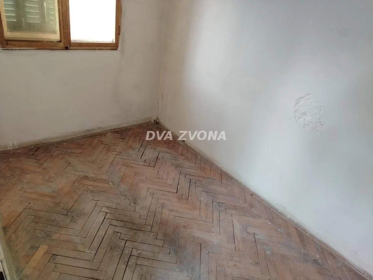 Prazna prostorija sa parketom i prozorom u uglu.