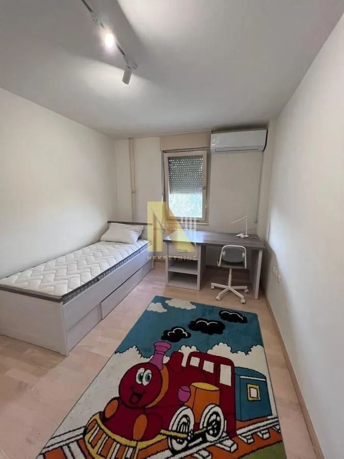 Dečja soba sa krevetom, radnim stolom i tepihom sa motivom voza.