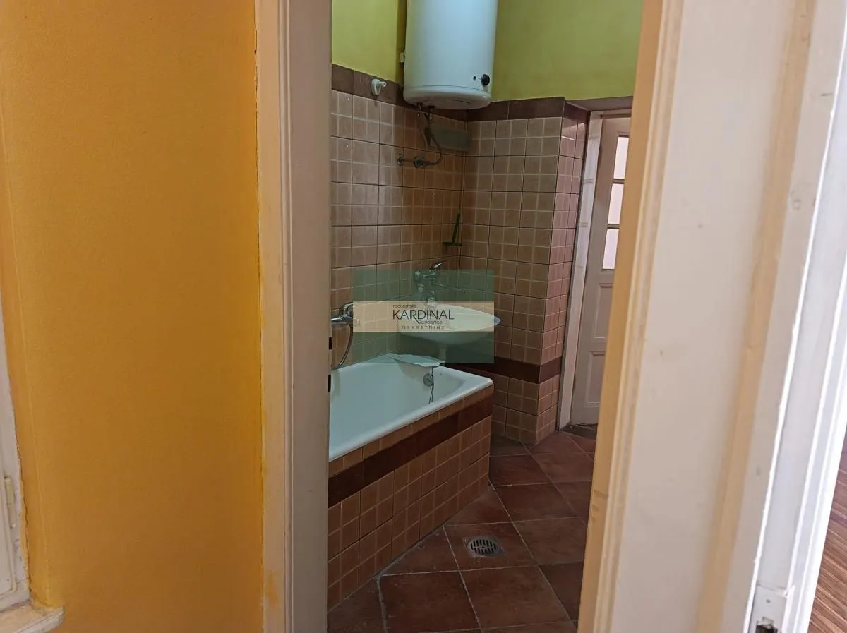 Pogled na kupatilo obloženo keramičkim pločicama sa kadom i bojlerom.