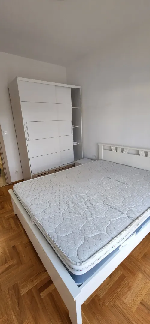 Svijetla spavaća soba sa bijelim krevetom i ormarom.