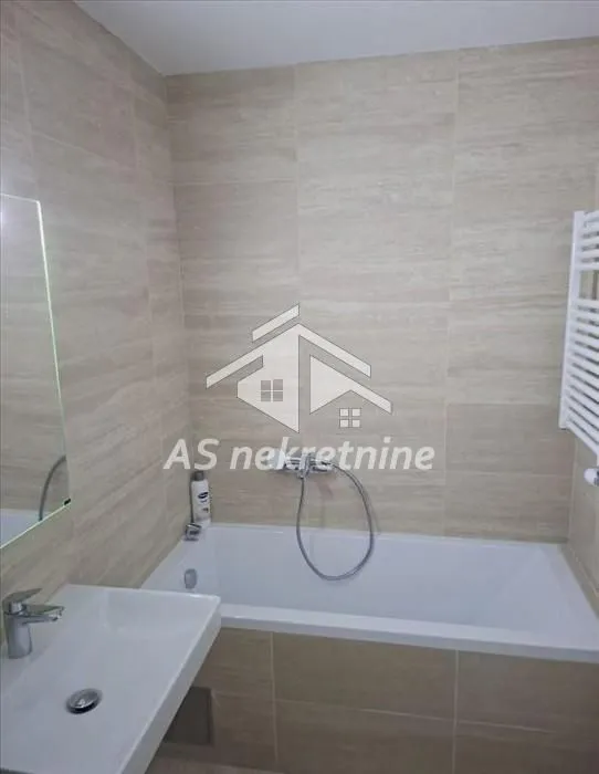 Bathroom equipped with a bathtub, washbasin, and neutral-toned tiles.