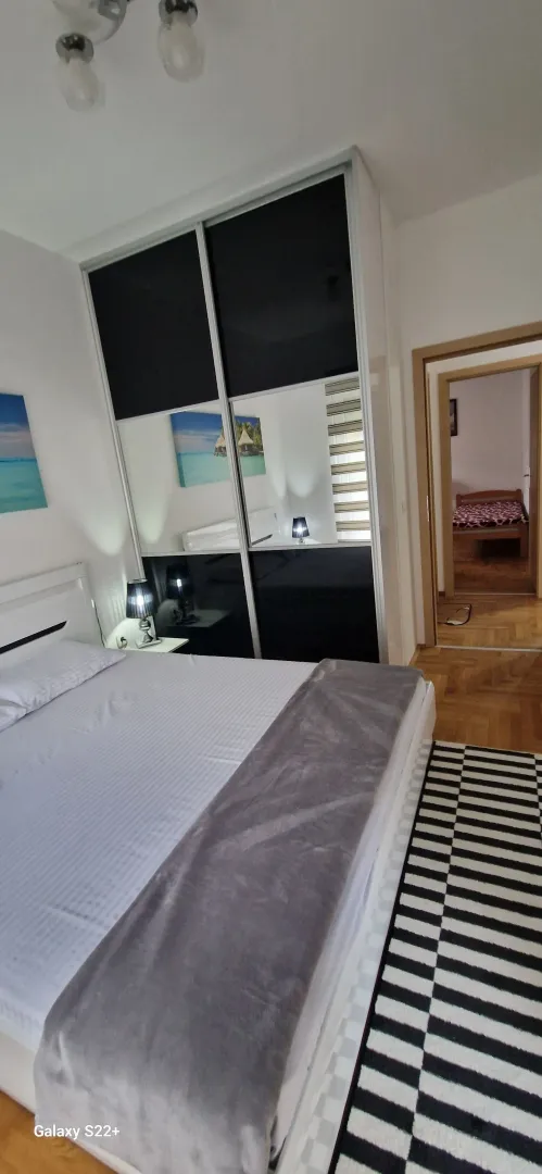 Furnished bedroom with a large double bed, mirrored wardrobe, and a view of another room.