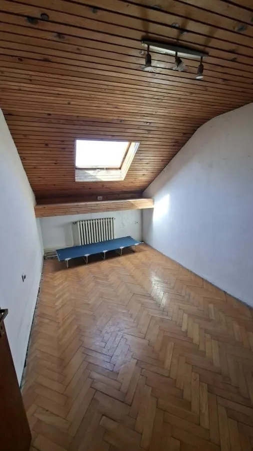 Prazna potkrovna soba sa drvenim krovom, parketom i krovnim prozorom.