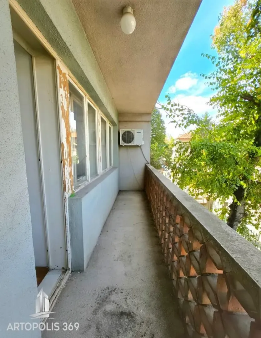 Dugačak natkriveni balkon sa pogledom na zelenilo i okolne zgrade.
