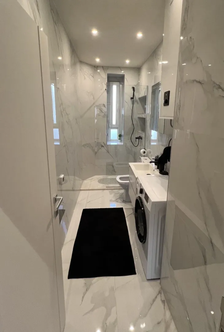 Modern bathroom with white marble tiles and a washing machine.