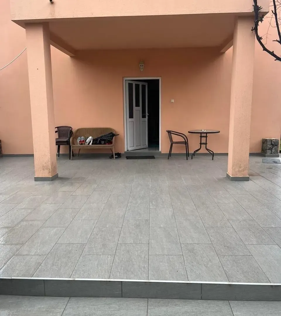 Natkrivena terasa sa popločanim podom i ulaznim vratima kuće.