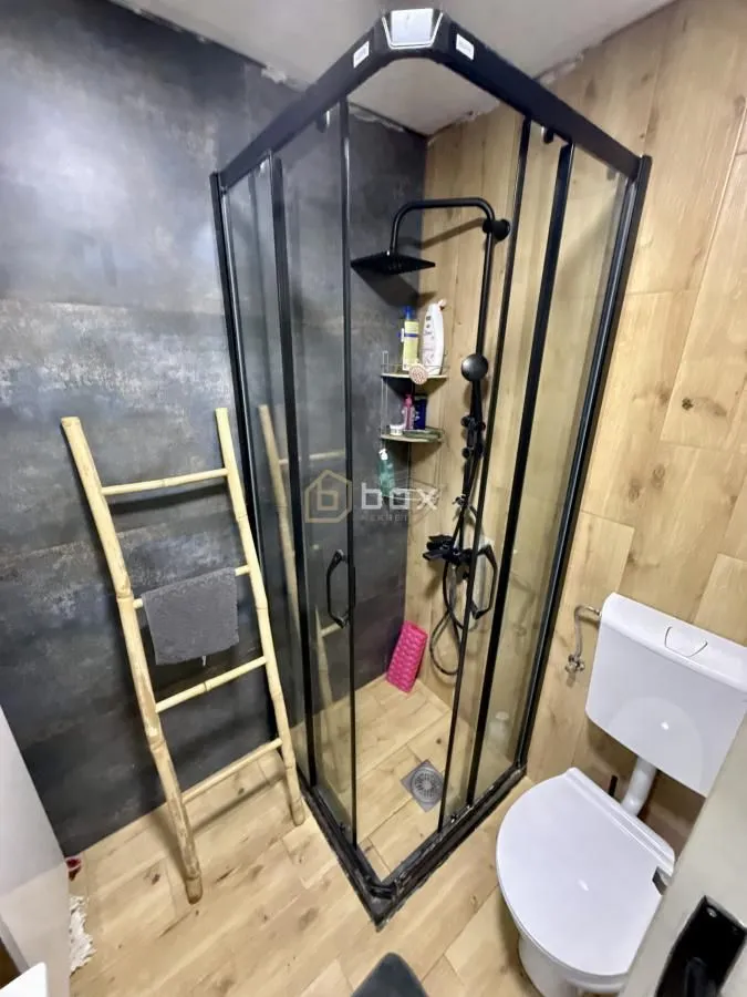 Kupatilo sa tuš kabinom, wc šoljom i dekorativnim drvenim detaljima.