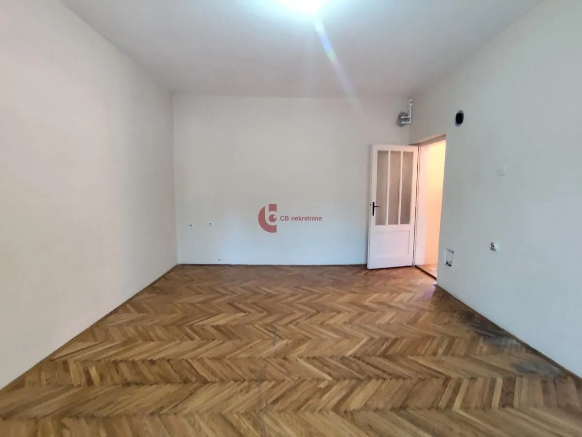Prazna prostorija sa parketom i belim zidovima.