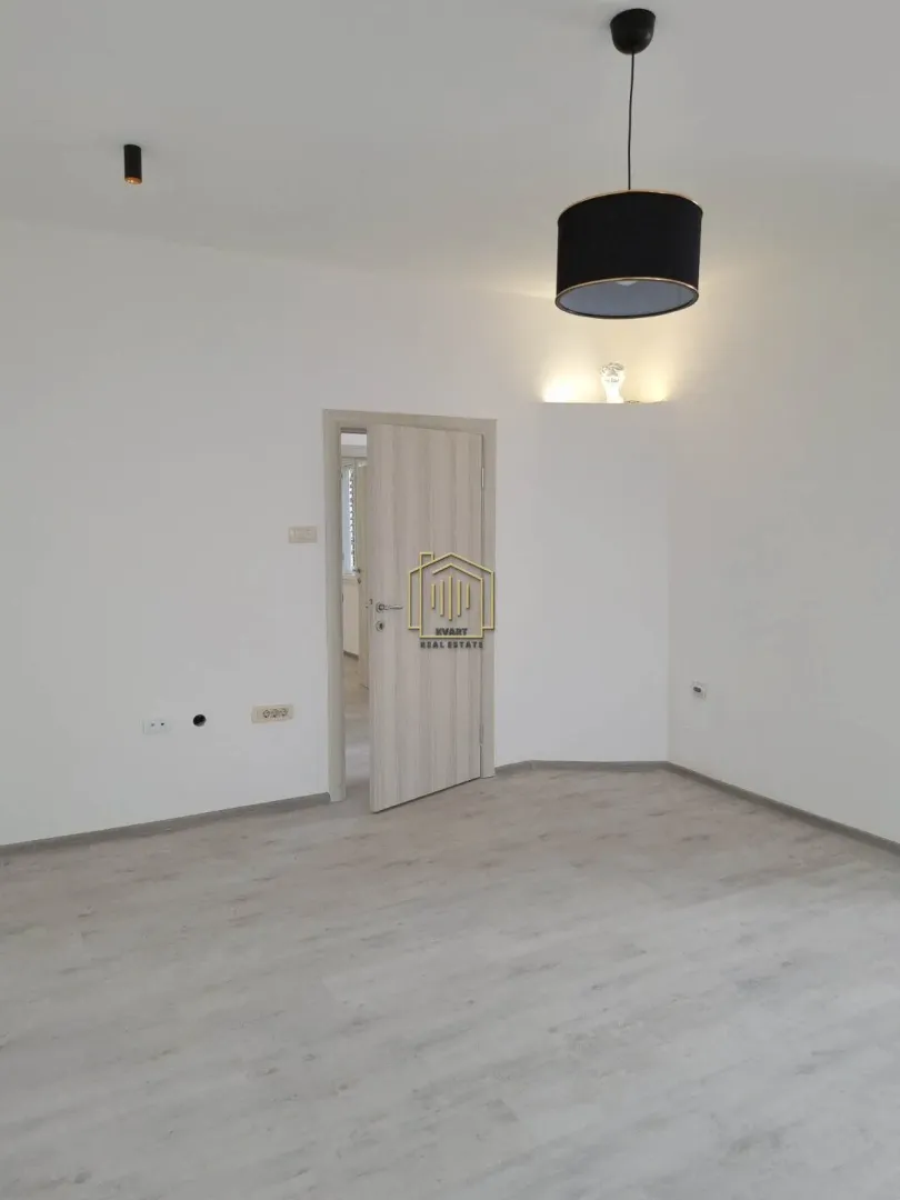 Empty room with light laminate flooring, white walls, and a wooden door.