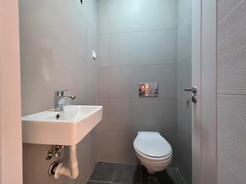 Manje kupatilo sa umivaonikom i toalet šoljom, obloženo sivim pločicama. - image 5