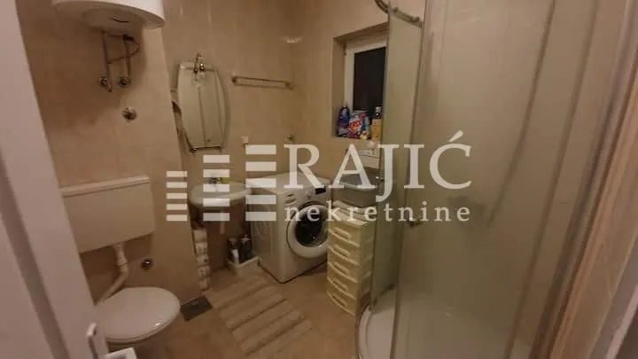 Smaller bathroom with a shower cabin, sink, toilet, and washing machine.