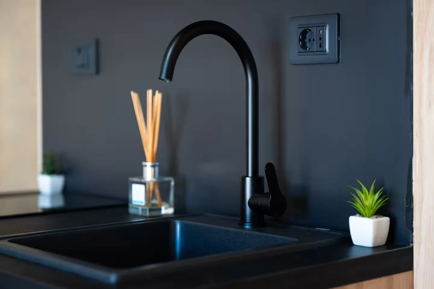 Moderna crna sudopera sa slavinom na tamnoj radnoj površini.