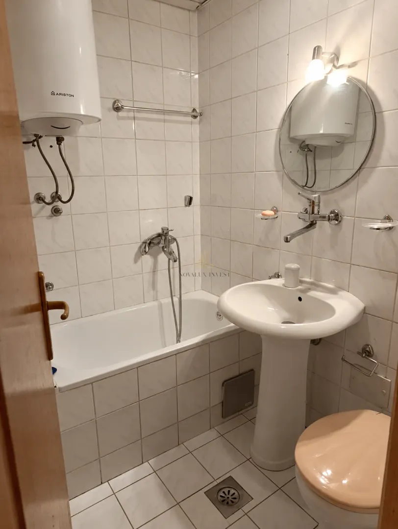 Kompaktno kupatilo sa kadom, umivaonikom i wc šoljom obloženo svijetlim pločicama.