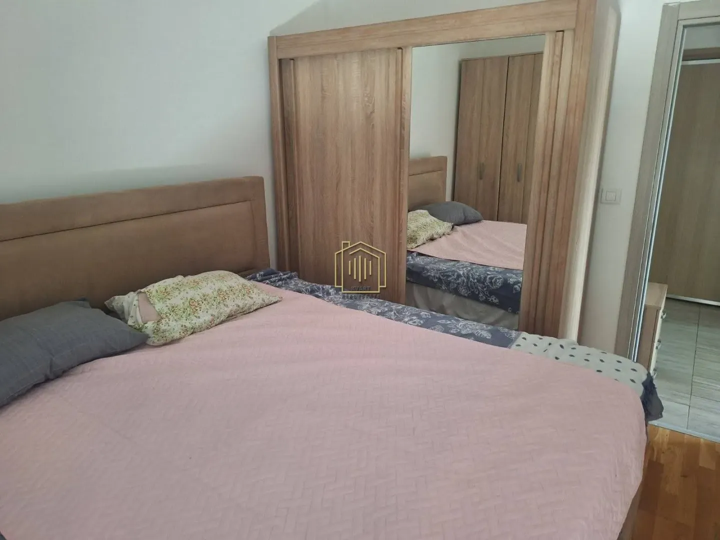 Furnished bedroom with a double bed and a wooden wardrobe with a mirror.