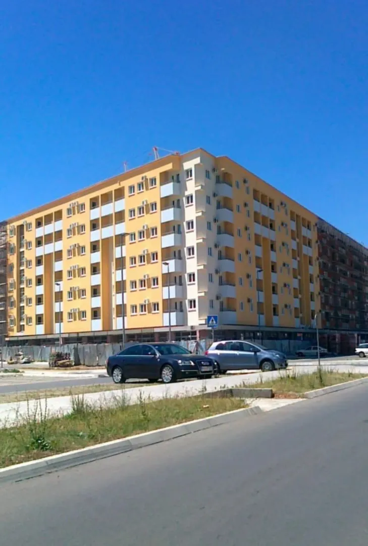 Pogled na spoljašnjost stambene zgrade sa parkiranim automobilima ispred.