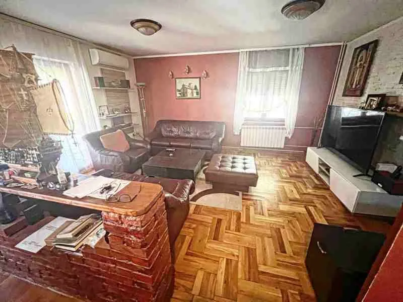 Dnevna soba sa garniturom za sedenje, drvenim podom i televizorom.